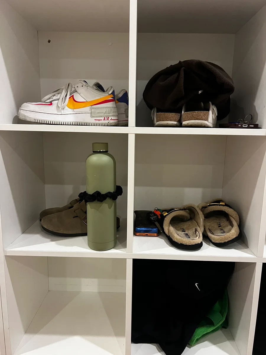 A sage-green water bottle wrapped with a black Kova Silk scrunchie on a shelf of shoes and accessories