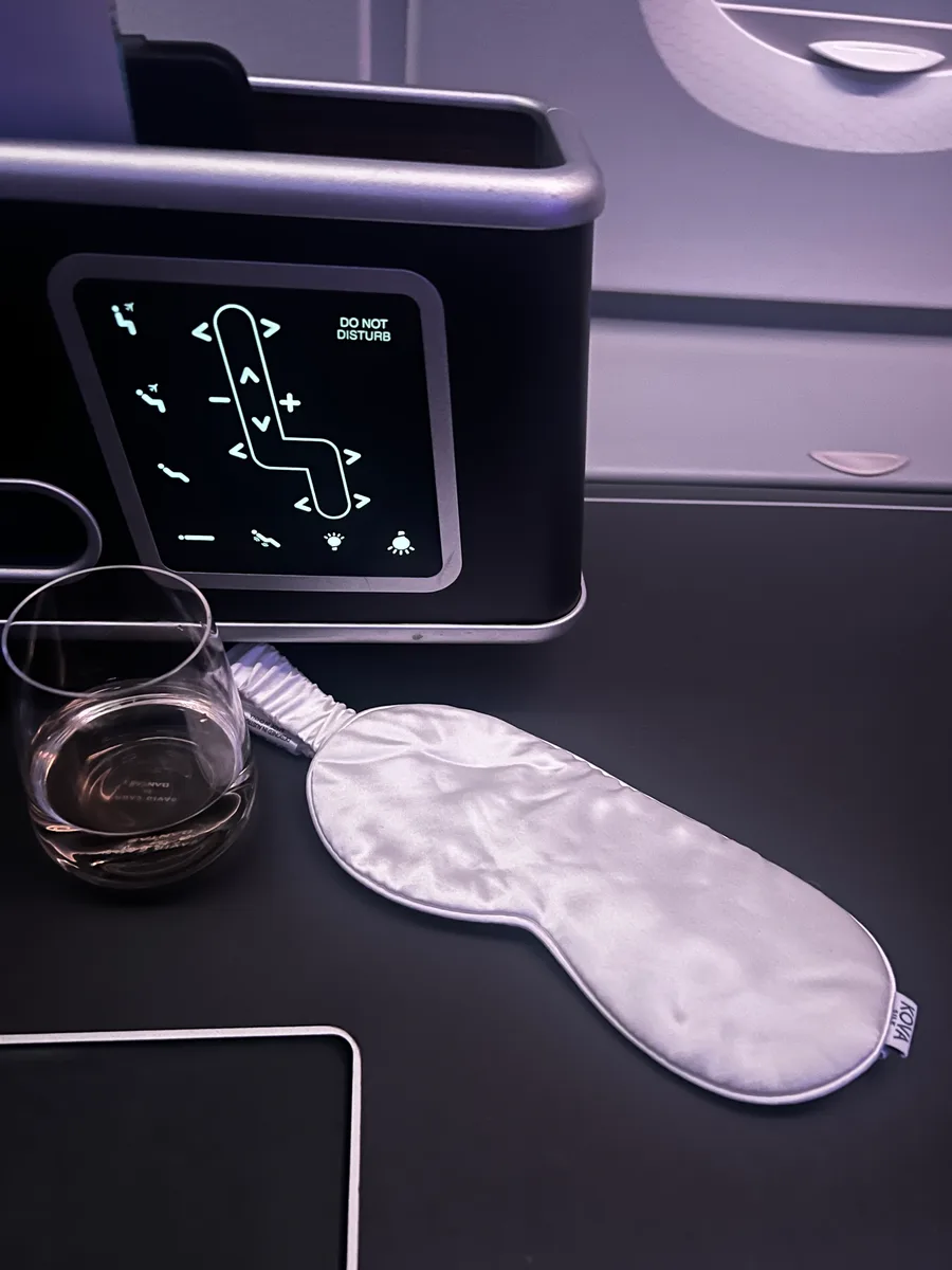 A white Kova Silk sleep mask and a glass of water on an airplane tray table